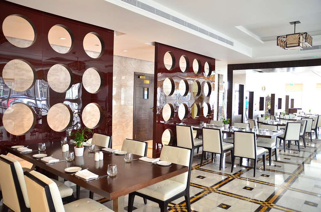Hotel Jannah Burj Al Sarab Abu Dhabi Esterno foto The photo shows a modern restaurant interior. It features a series of tables with elegant place settings and comfortable chairs. The walls are decorated with a unique design, displaying round mirrors or circular elements set in a polished brown panel