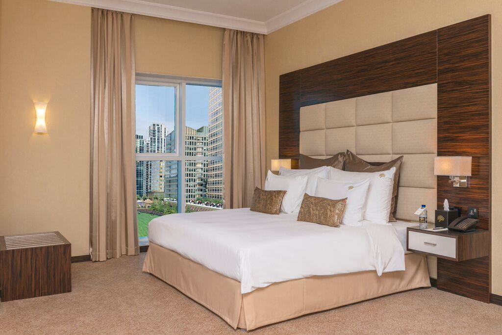 Hotel Jannah Burj Al Sarab Abu Dhabi Esterno foto The photo shows a well-decorated hotel room featuring a large bed with white bedding and decorative pillows. The walls are painted in a warm color, and there are modern wooden accents. On one side, there are light fixtures, and beside the bed, there 